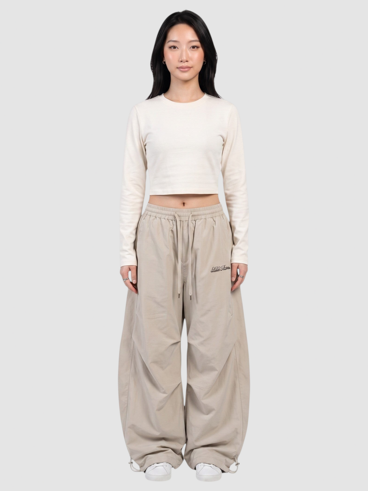 Y2K Avenue beige oversized nylon joggers with elastic waistband and white script logo, worn by a model.