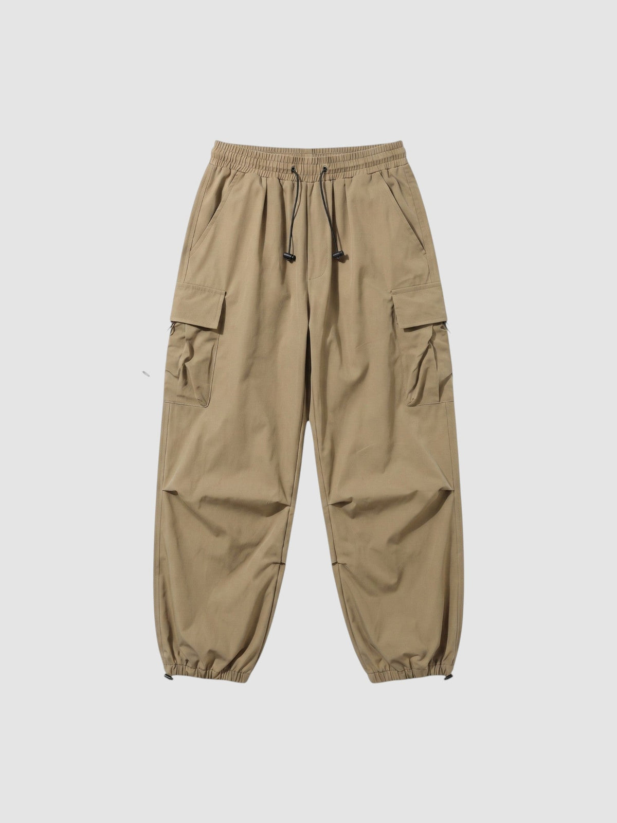 Pantalon cargo parachute beige avec taille élastique, cordons aux chevilles et poches à rabat sur les côtés, en tissu mat.