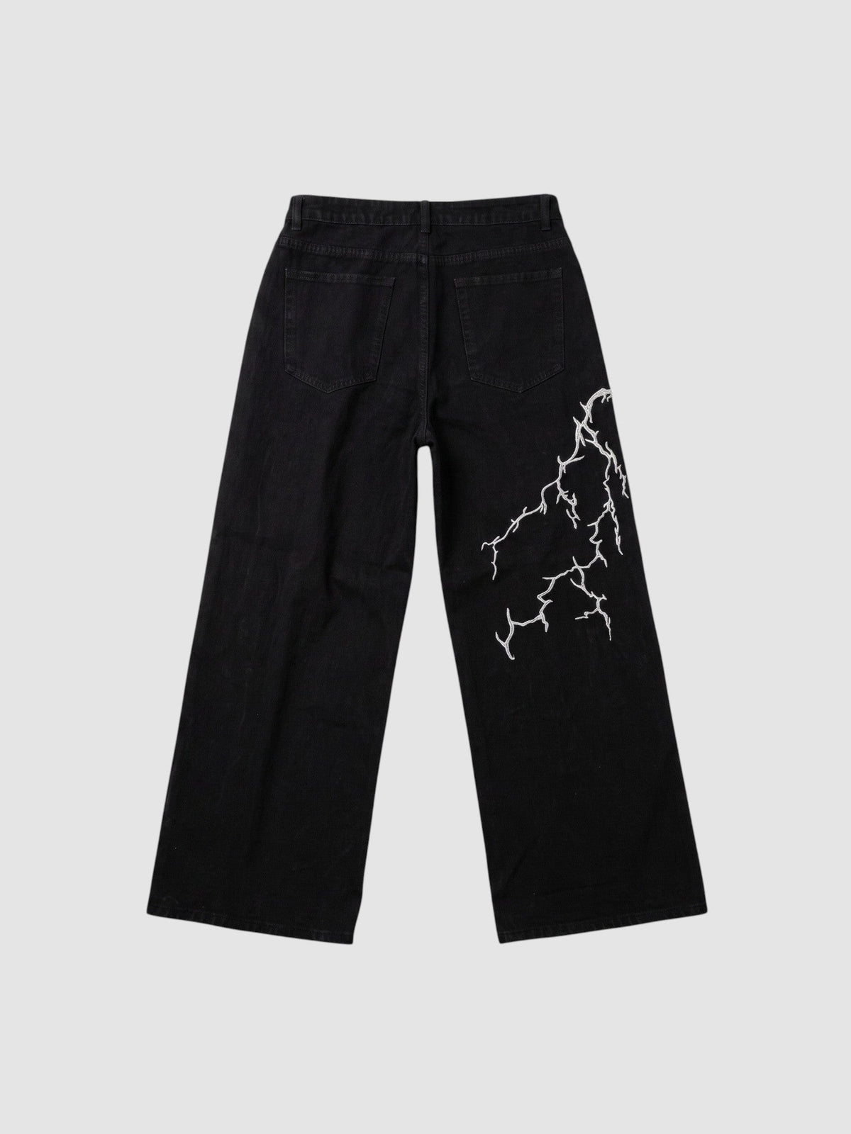 Jean en denim noir jambe large avec broderie éclair blanche asymétrique sur la jambe arrière.