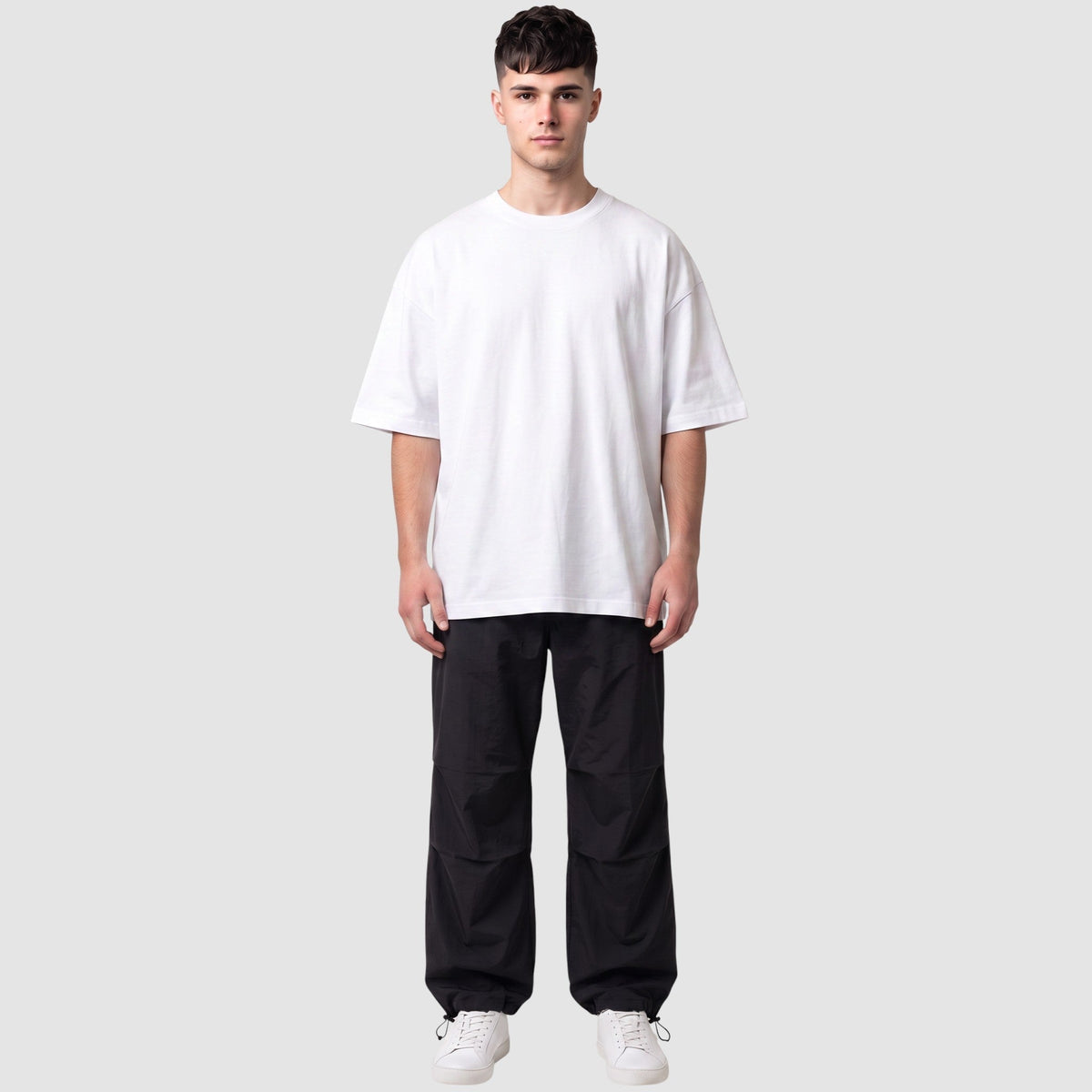 Pantalon parachute noir avec taille élastique et chevilles ajustables, porté par un modèle homme en t-shirt blanc.