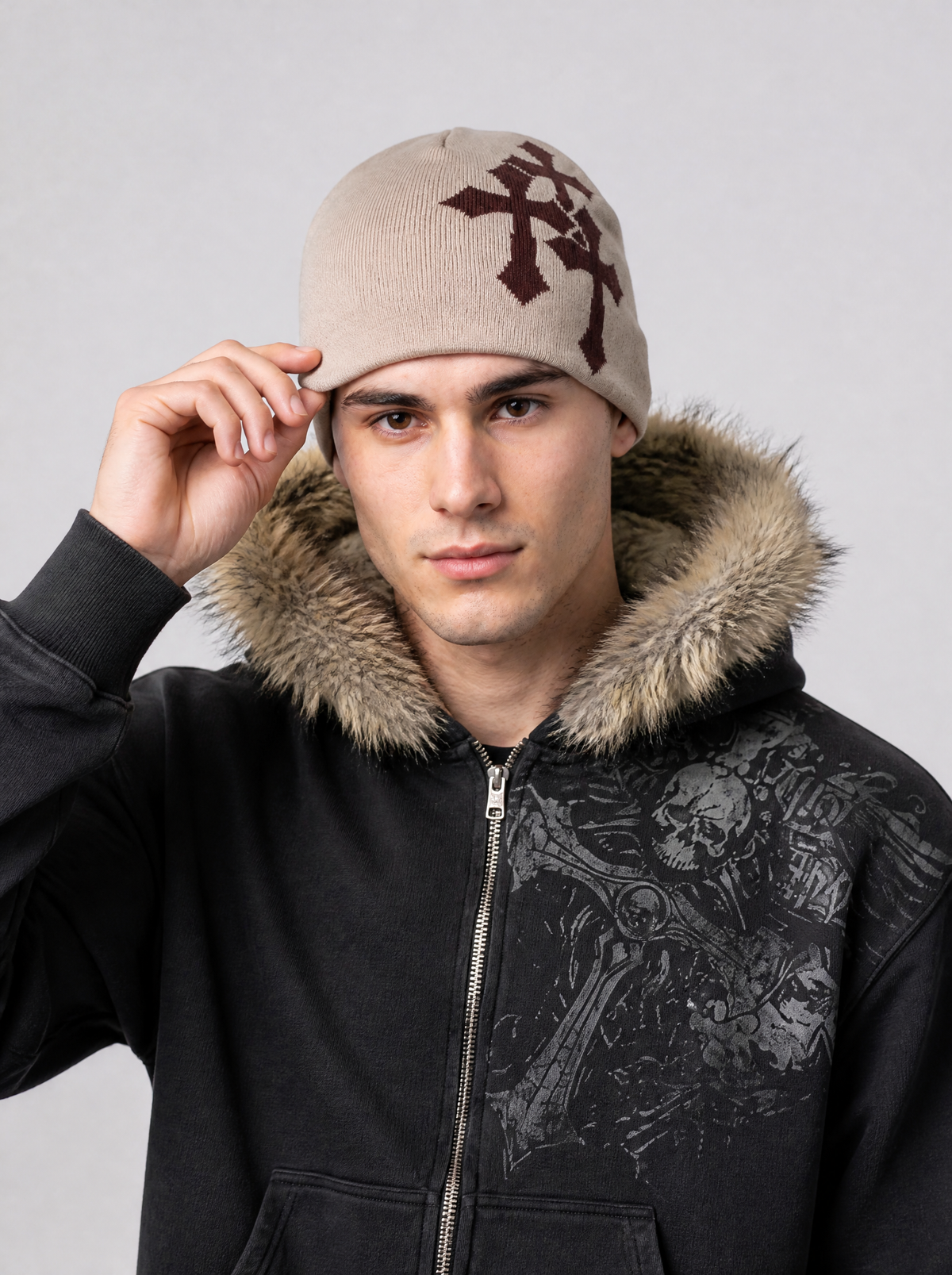 Autre vue | Homme de face touchant son bonnet beige à croix gothiques bordeaux, veste zippée noire à capuche fourrée | Variante : Beige