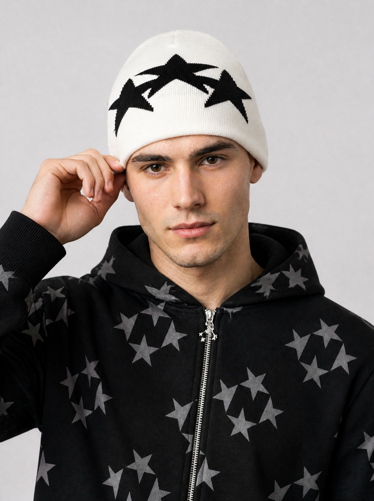 Autre vue | Homme de face, main sur son bonnet blanc à trois grandes étoiles noires, veste zippée noire étoilée | Variante : Blanc