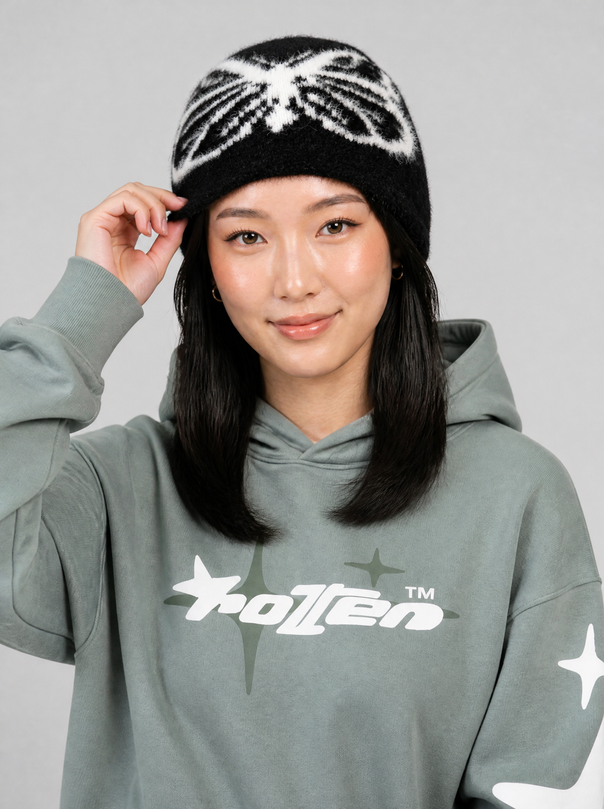 Autre vue | Femme de face, main sur son bonnet noir en maille poilue à motif papillon blanc, hoodie vert sauge | Variante : Noir