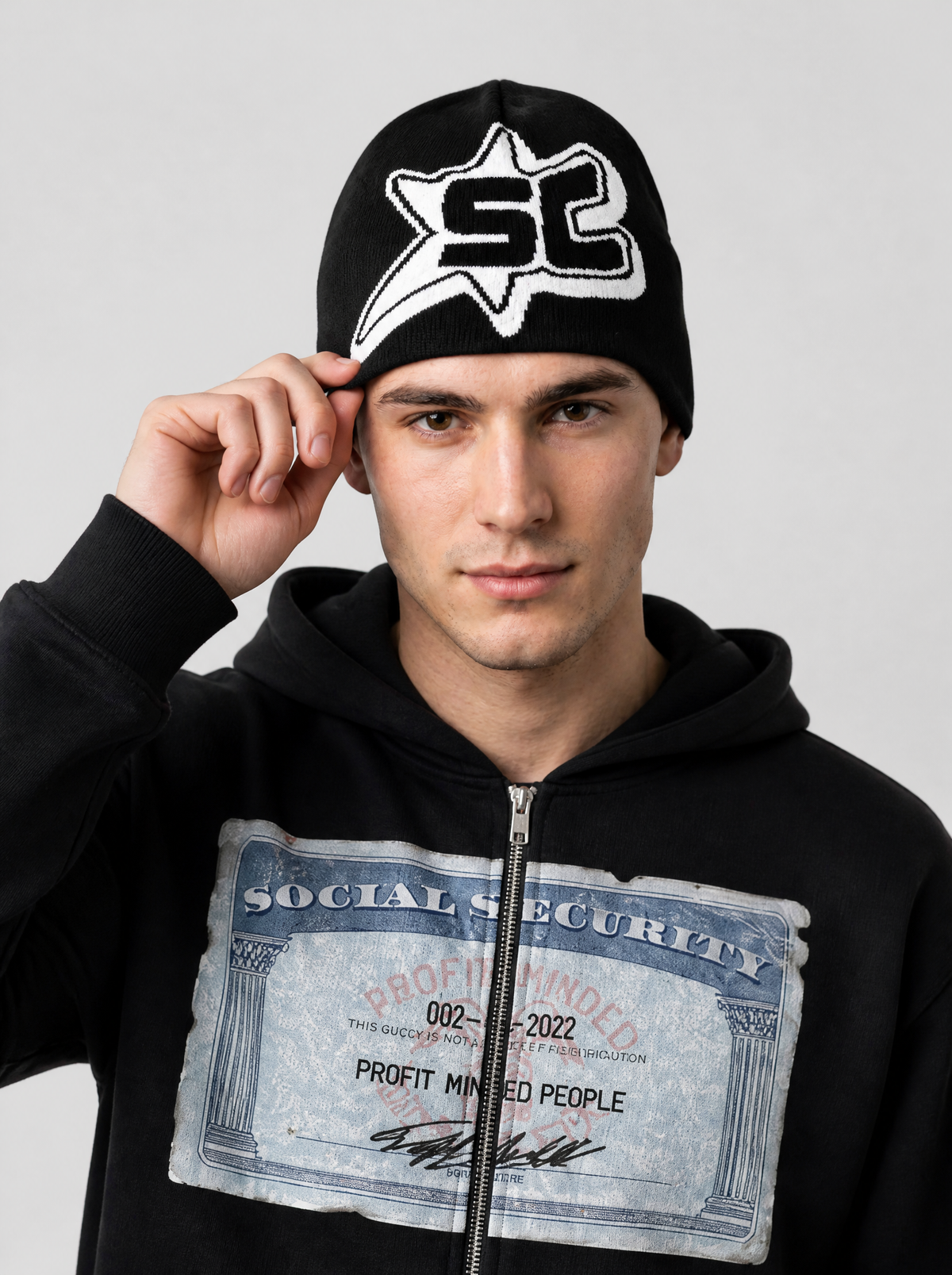 Autre vue | Homme de face, main sur son bonnet noir à badge étoile blanc SC, sweat zippé noir imprimé carte | Variante : Noir