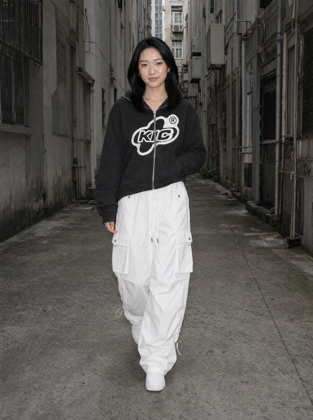 Photo lifestyle | Pantalon cargo parachute blanc à poches à rabat porté par une femme qui marche dans une ruelle, avec un sweat zippé noir