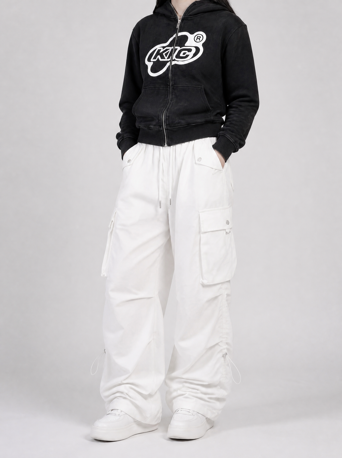 Autre vue | Pantalon cargo parachute blanc à poches à rabat porté de trois quarts avec un sweat zippé noir délavé à logo