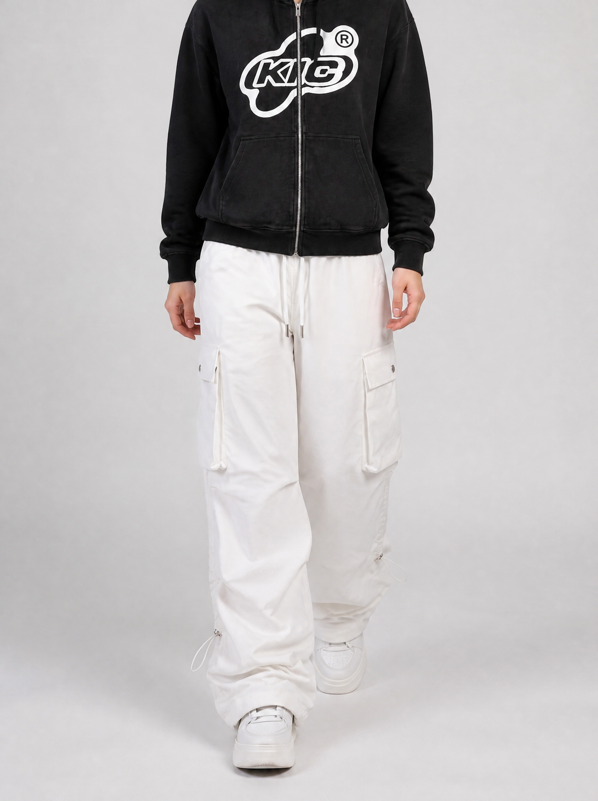Autre vue | Femme qui marche en cargo parachute blanc large à cordons de serrage, sweat zippé noir à logo blanc