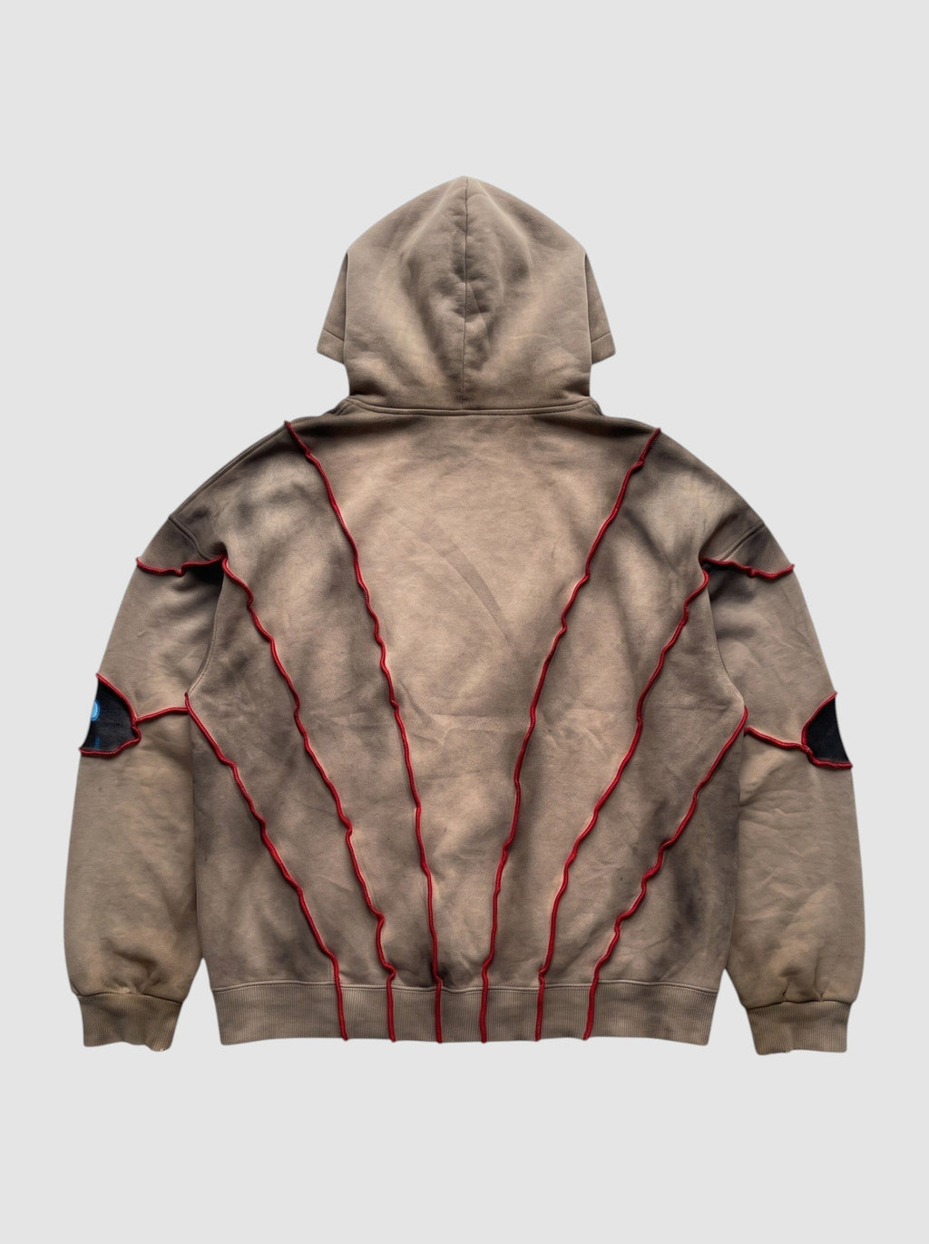 Hoodie beige délavé coupe boxy avec coutures en relief rouges et détails patchwork en forme d'yeux au dos.