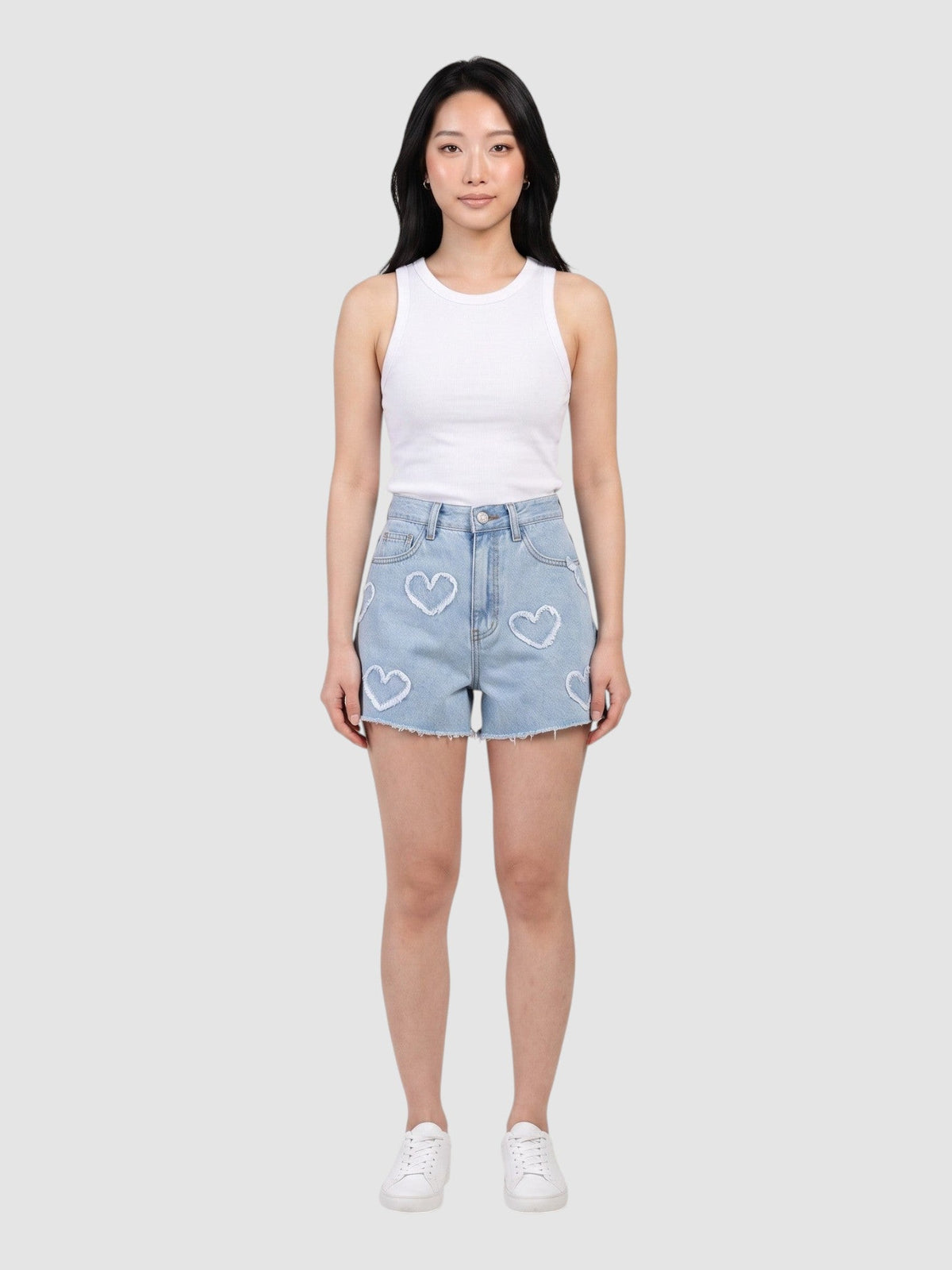 Modèle portant un short en denim bleu clair taille haute avec appliqués cœur effrangés et ourlet brut.