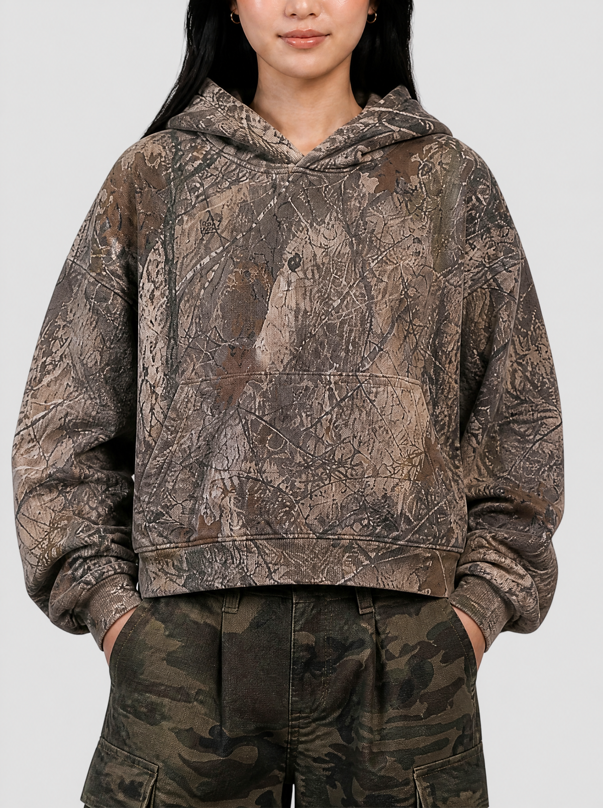 Photo détail | Gros plan sur l’imprimé camouflage écorce et feuillage, la poche kangourou et les bords côtelés du hoodie