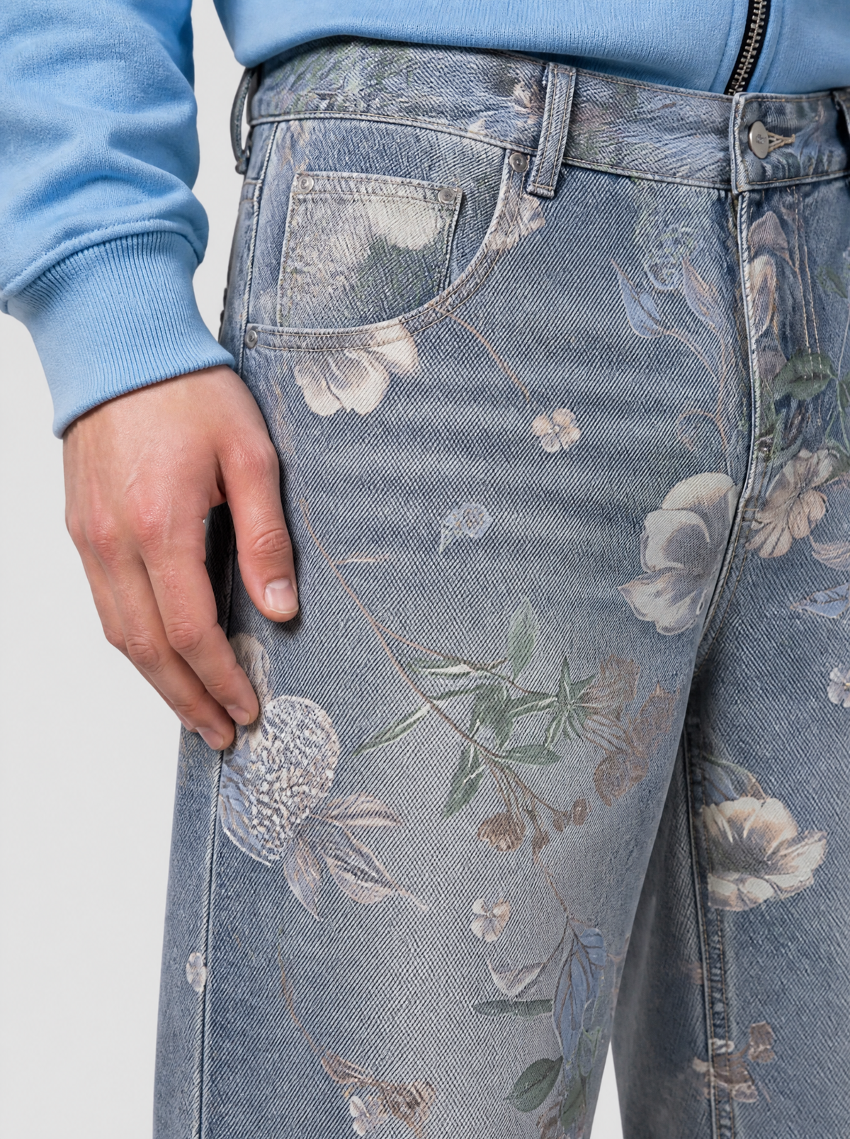 Photo détail | Gros plan sur l'imprimé fleuri du jean bleu clair : fleurs crème, grappes blanches et feuilles vertes près de la poche avant