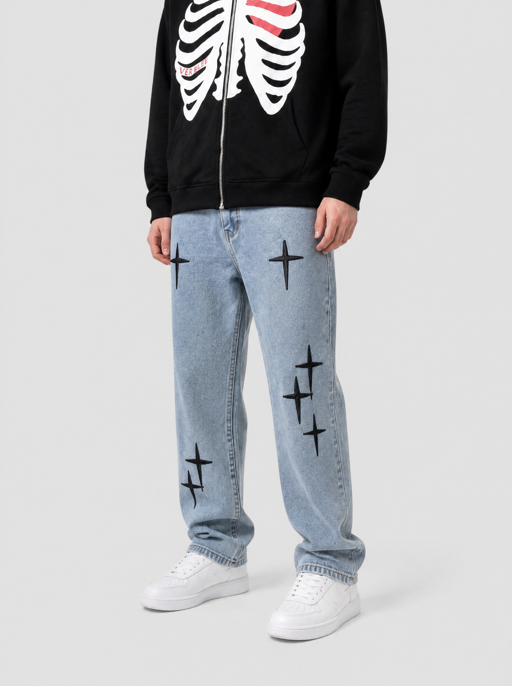 Autre vue | Jean droit bleu clair délavé brodé de croix noires, porté de trois quarts face avec un hoodie zippé noir à cage thoracique blanche