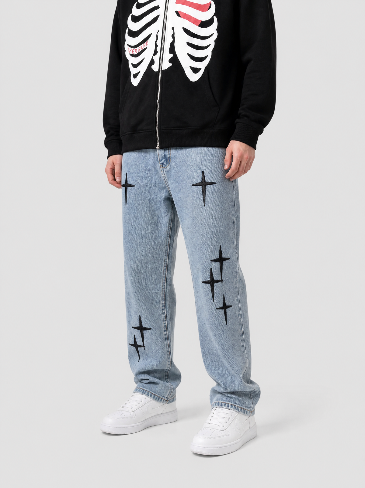 Autre vue | Jean droit bleu clair délavé brodé de croix noires, porté de trois quarts face avec un hoodie zippé noir à cage thoracique blanche