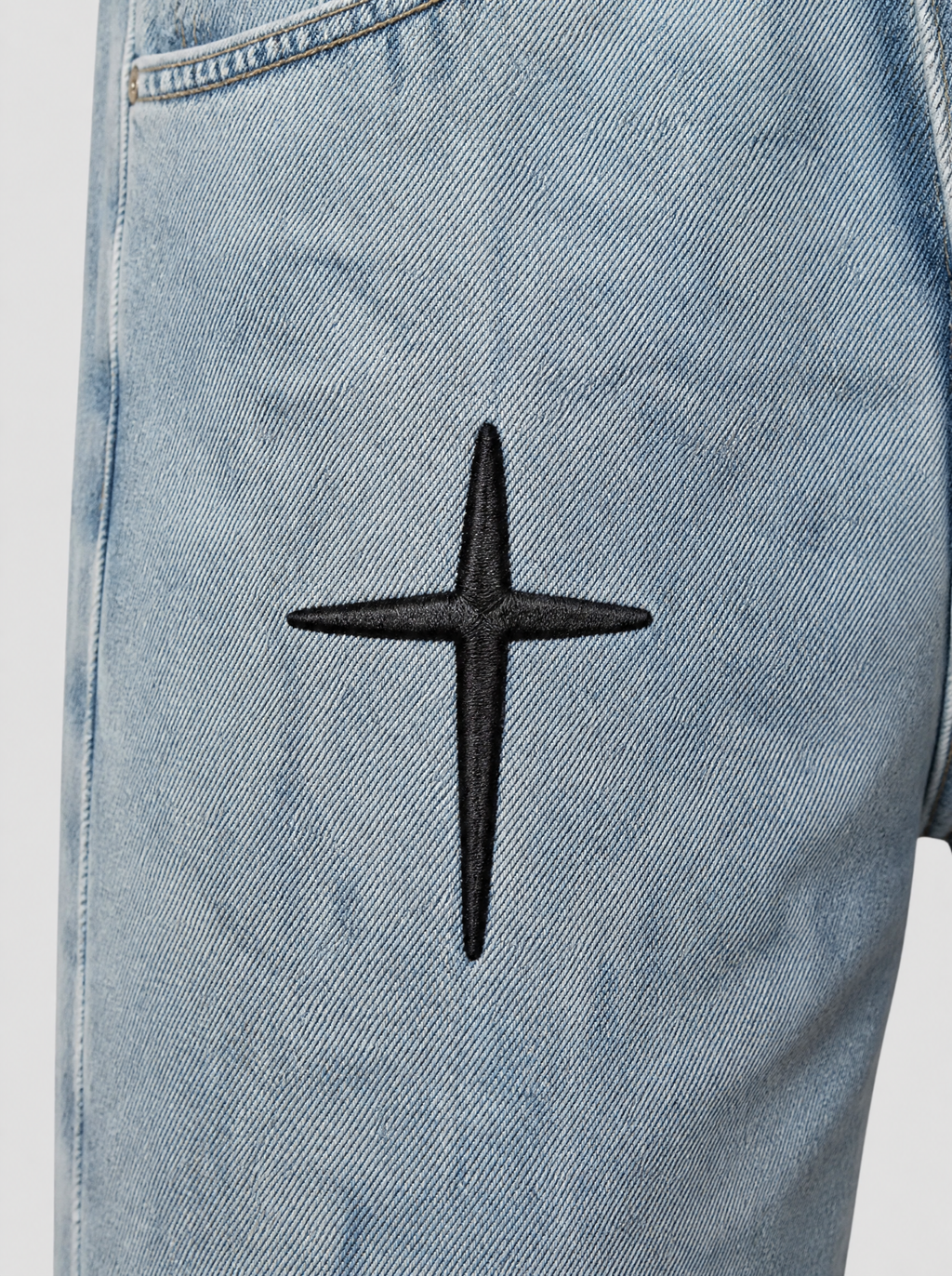 Photo détail | Gros plan sur les croix gothiques noires brodées sur la cuisse du jean bleu clair délavé, texture du fil bien visible