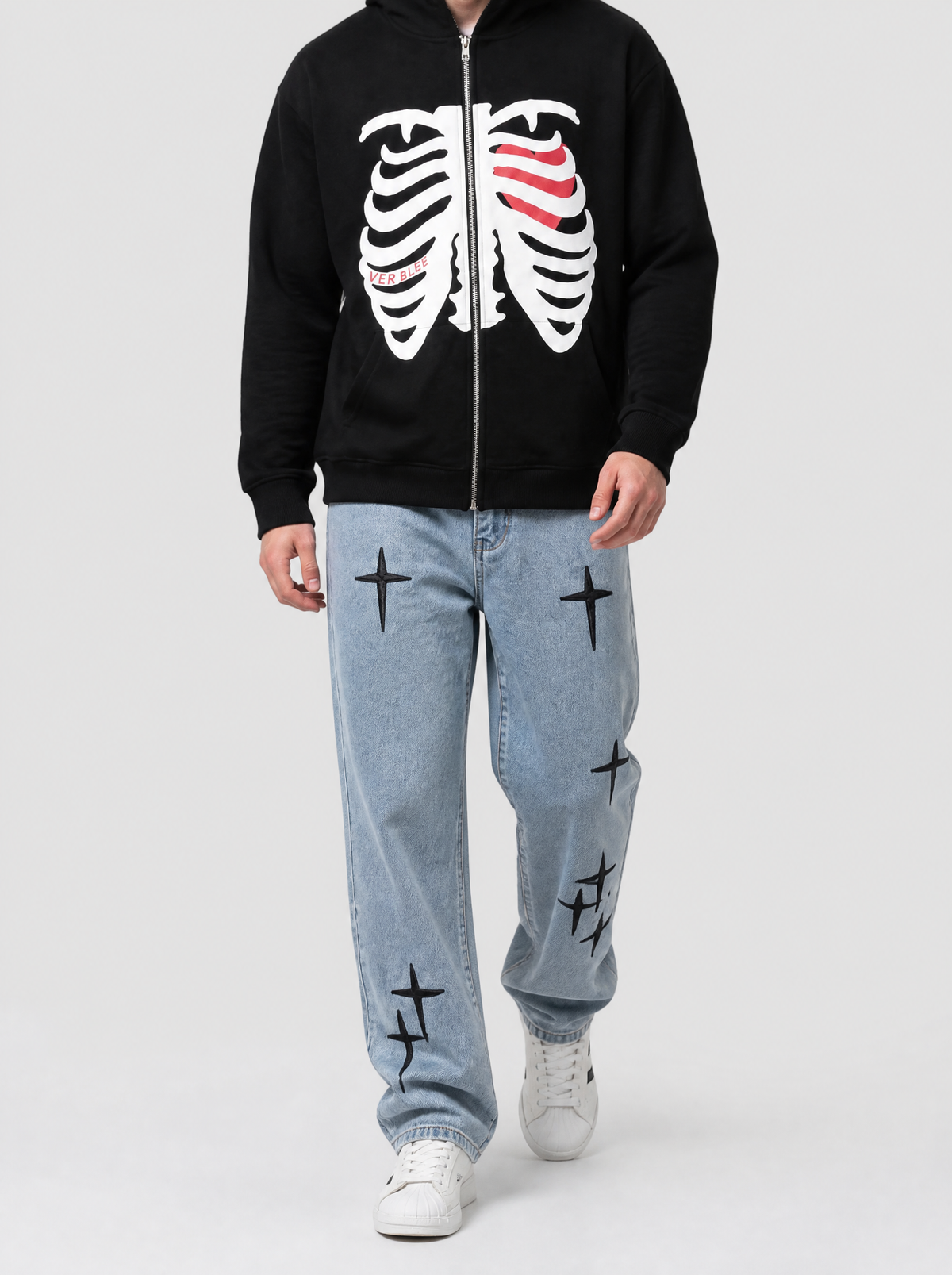 Autre vue | Homme marchant de face en jean bleu clair à croix gothiques noires brodées, assorti à un hoodie zippé noir imprimé squelette