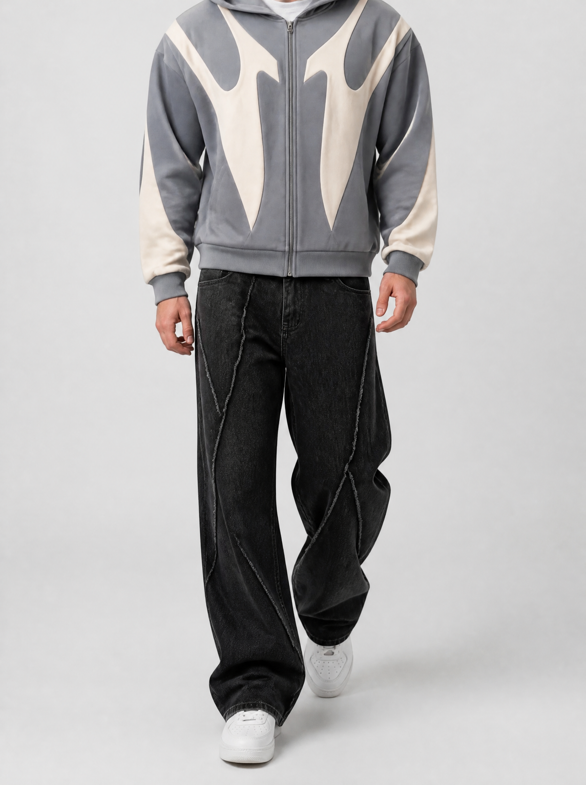 Autre vue | Homme marchant de face en jean noir ample aux coutures spirales effilochées, avec un hoodie zippé gris aux motifs crème incurvés