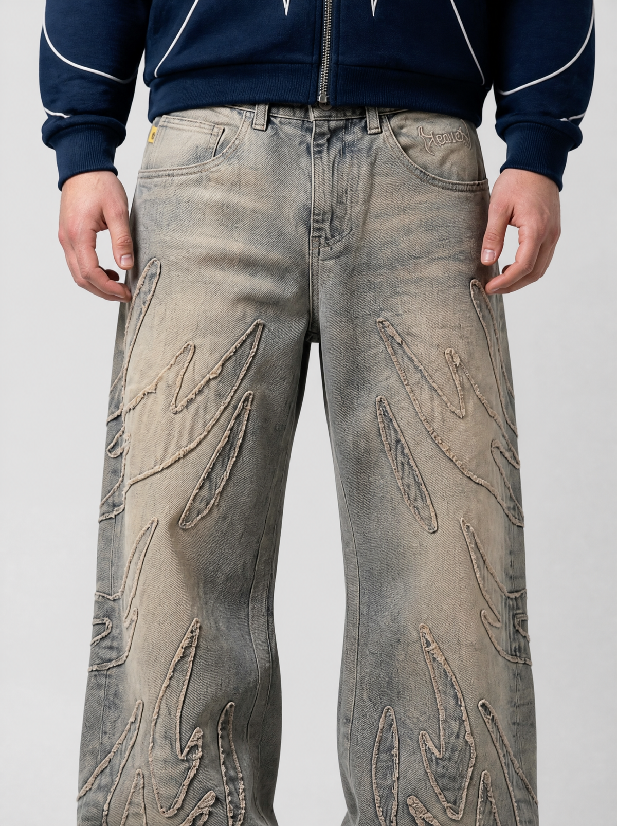 Photo détail | Gros plan sur les flammes appliquées aux bords effilochés sur la cuisse du jean gris délavé teinté de beige | Variante : Gris