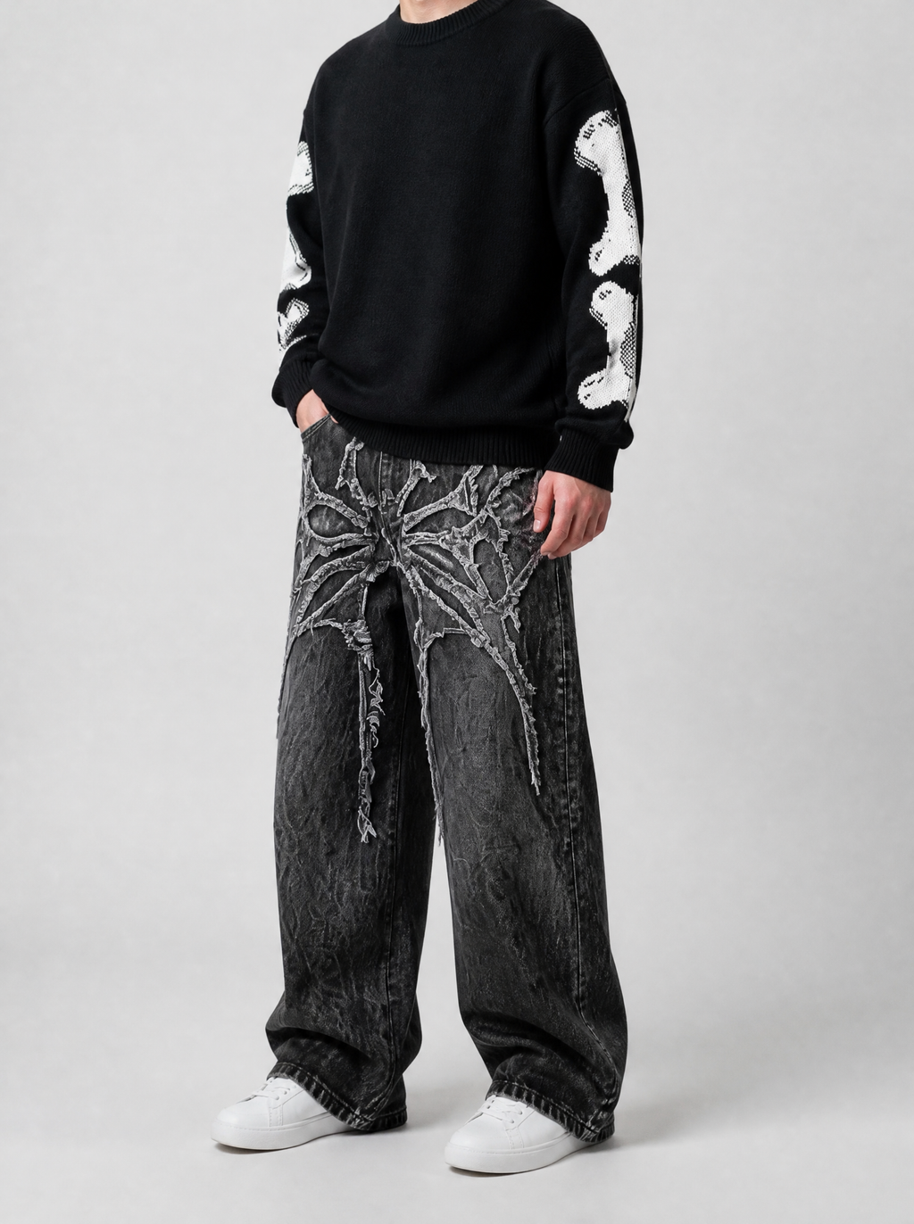 Autre vue | Jean baggy noir à délavage craquelé et appliqué gothique épineux, porté de trois quarts face avec un pull noir aux manches os