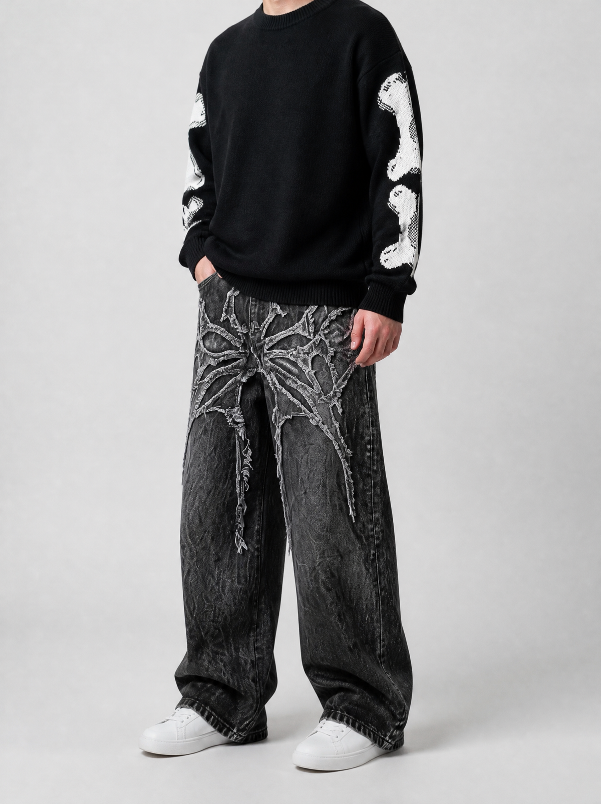 Autre vue | Jean baggy noir à délavage craquelé et appliqué gothique épineux, porté de trois quarts face avec un pull noir aux manches os