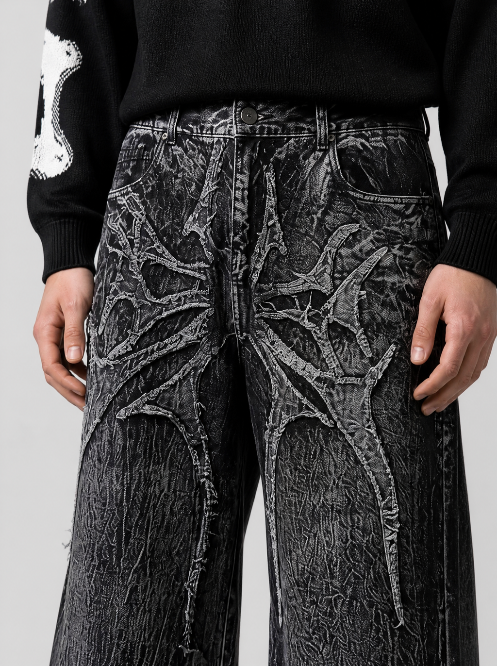 Photo détail | Gros plan sur l'appliqué gothique épineux en relief sur les cuisses du jean noir au délavage marbré blanc
