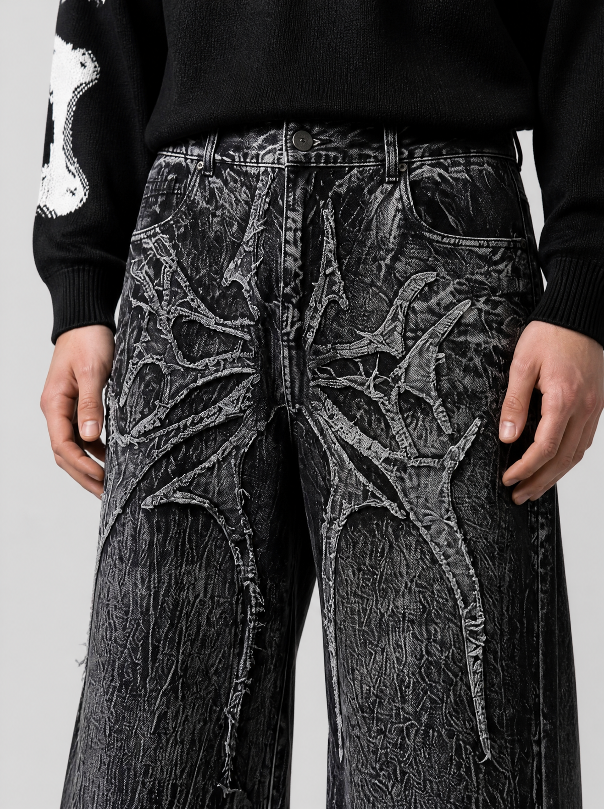 Photo détail | Gros plan sur l'appliqué gothique épineux en relief sur les cuisses du jean noir au délavage marbré blanc