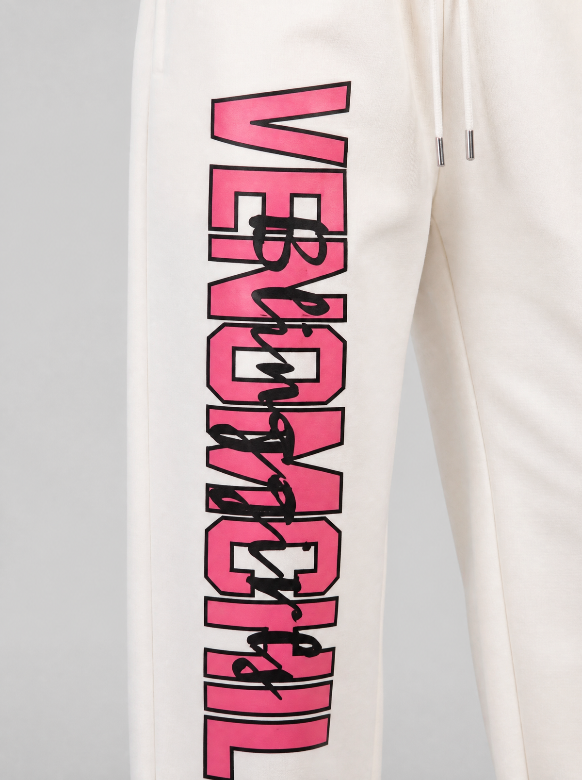 Photo détail | Gros plan sur le lettrage rose VENOMCHILL contouré de noir et son écriture manuscrite noire sur la cuisse du jogging crème
