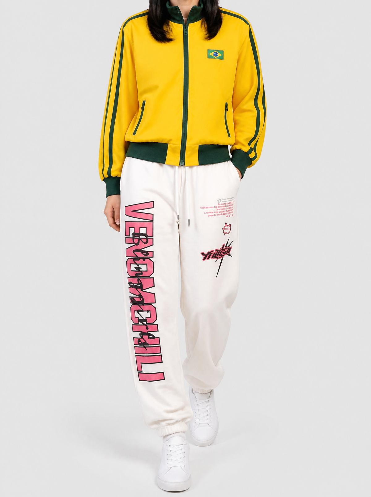 Autre vue | Femme marchant de face en jogging blanc cassé à lettrage rose et tag graffiti, avec une veste zippée jaune à bandes vertes
