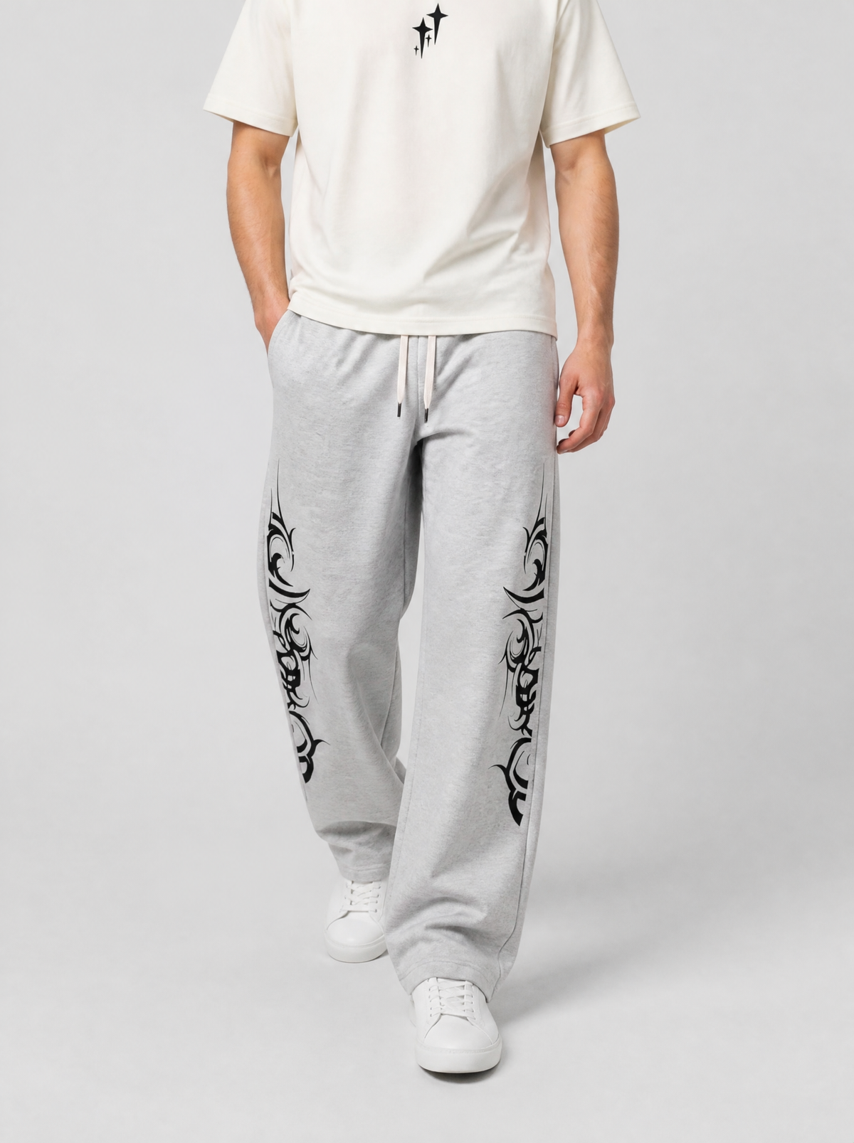 Autre vue | Homme marchant de face en jogging gris clair large orné de tatouages tribaux noirs, avec un t-shirt crème au motif minimaliste