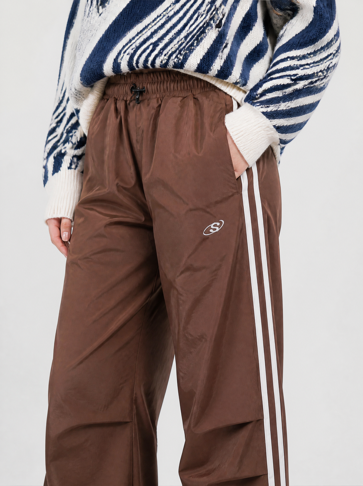 Photo détail | Gros plan sur la taille élastique, le cordon, le petit logo brodé et les deux bandes blanches du jogging marron | Variante : Marron