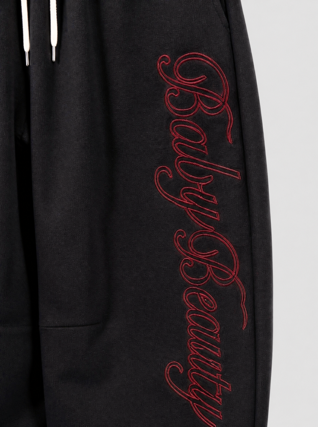 Photo détail | Gros plan sur la broderie calligraphiée rouge Baby Beauty qui descend le long de la cuisse du jogging noir | Variante : Noir