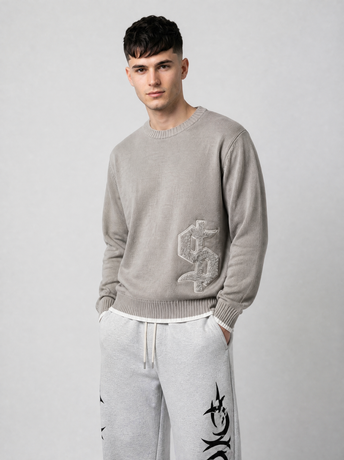 Autre vue | Pull en maille taupe à dollar gothique brodé en bas du devant, porté de trois quarts face avec un jogging gris à motifs tribaux