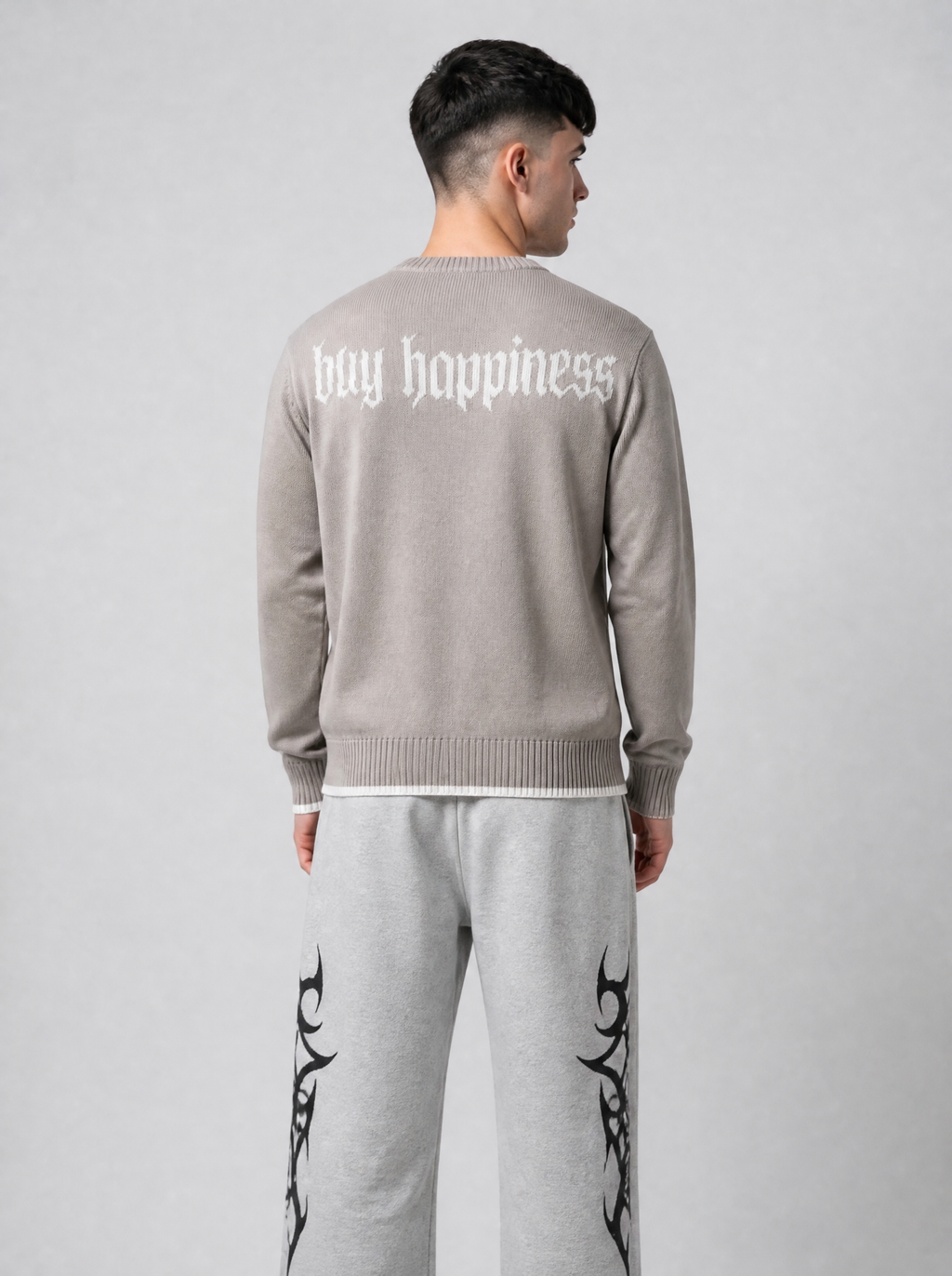Autre vue | Vue de dos du pull taupe avec l'inscription buy happiness en lettres gothiques blanches, porté avec un jogging gris chiné