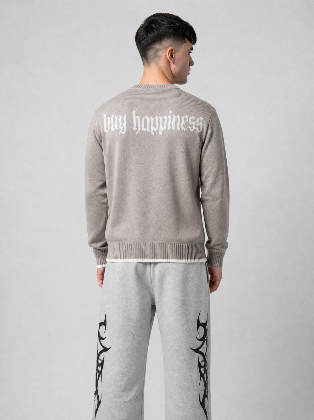 Autre vue | Vue de dos du pull taupe avec l'inscription buy happiness en lettres gothiques blanches, porté avec un jogging gris chiné