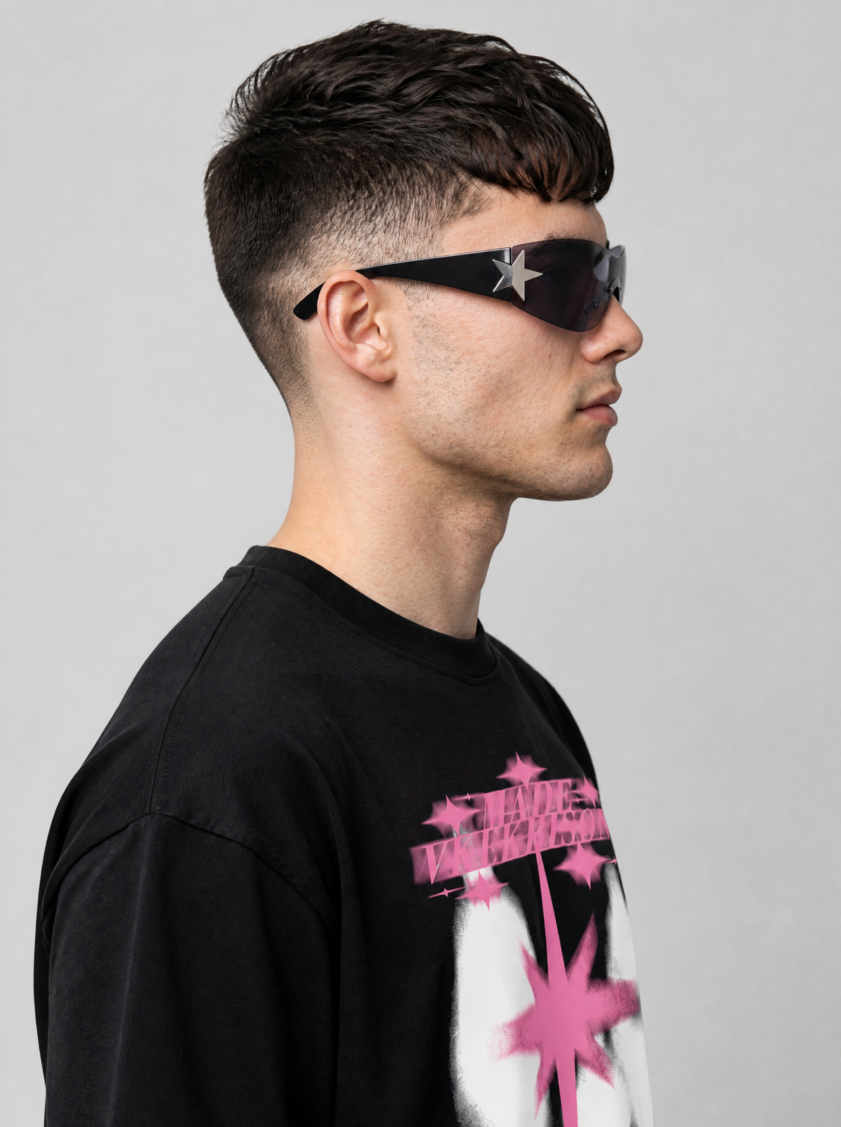 Autre vue | Vue de profil des lunettes masque noires avec étoile argentée à la charnière et verre gris, homme en t-shirt noir imprimé rose | Variante : Noir