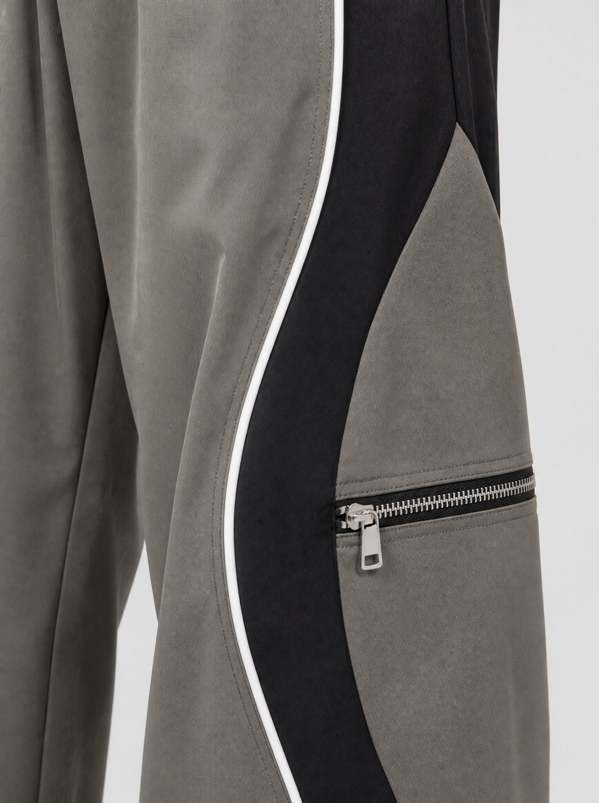 Photo détail | Gros plan sur le passepoil blanc ondulé entre le gris et le noir et sur la poche zippée argentée du pantalon