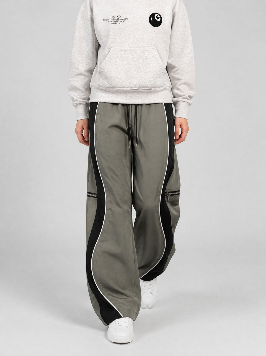 Autre vue | Femme marchant de face en pantalon large gris à bandes noires courbées, poches zippées aux genoux et hoodie gris chiné