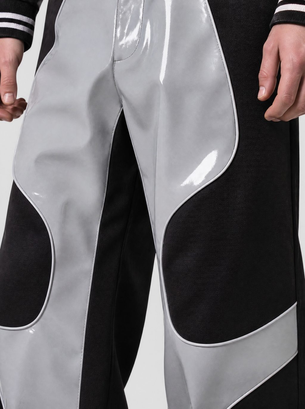 Photo détail | Gros plan sur la découpe courbée entre le simili cuir gris verni et le tissu noir mat du pantalon moto