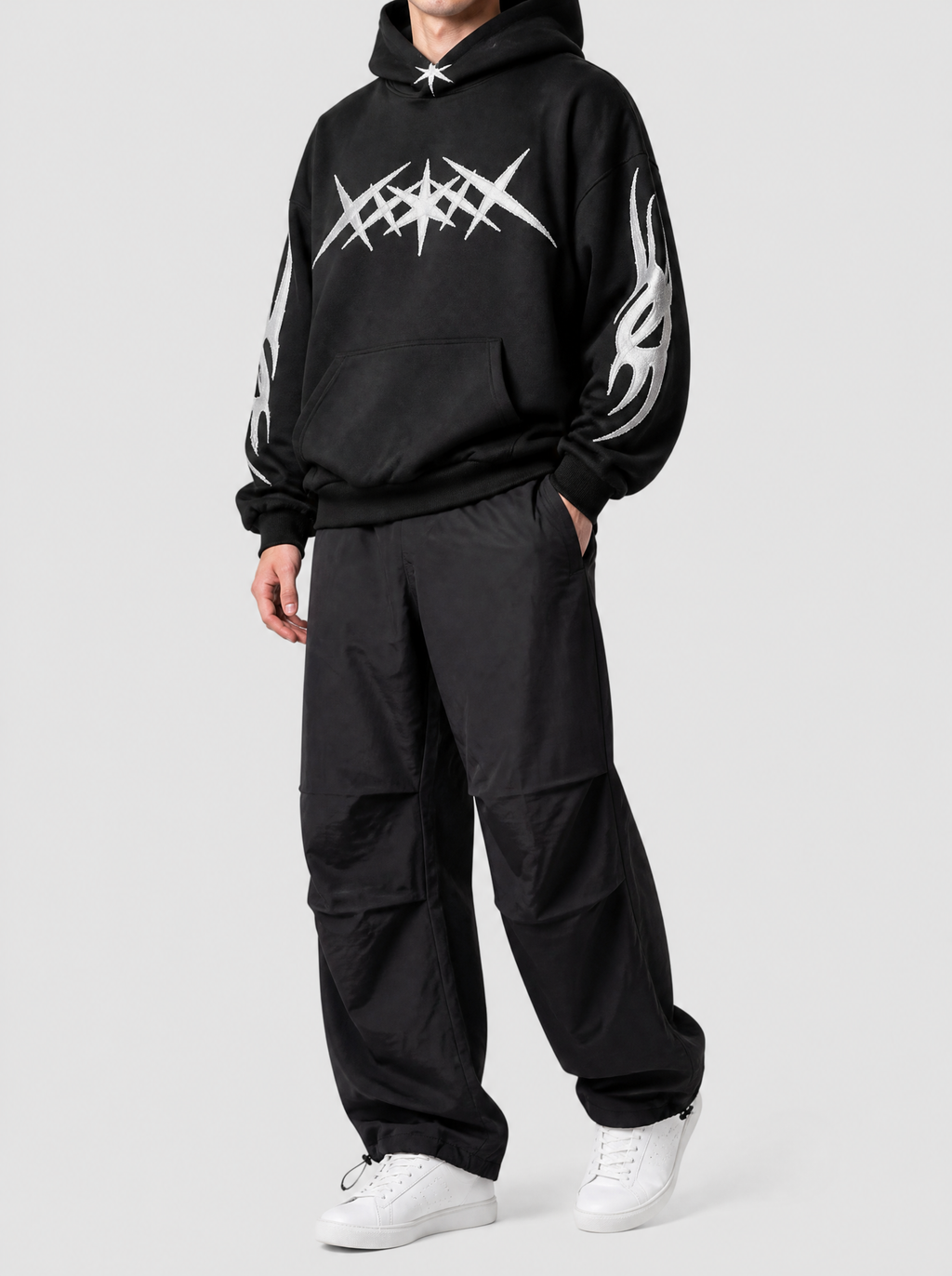 Autre vue | Pantalon parachute noir large en nylon léger à plis aux genoux, porté de trois quarts avec un hoodie noir à motif blanc