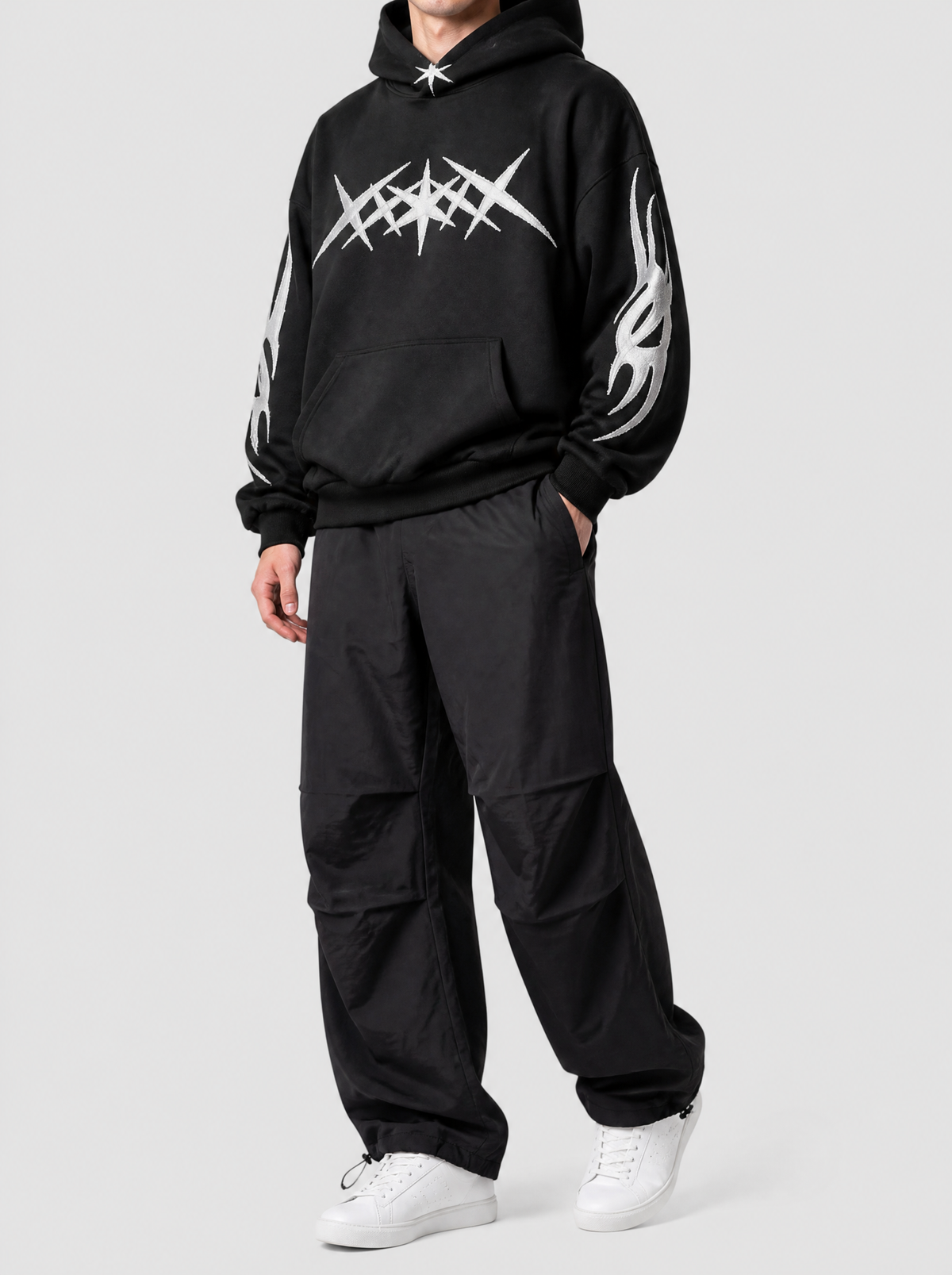 Autre vue | Pantalon parachute noir large en nylon léger à plis aux genoux, porté de trois quarts avec un hoodie noir à motif blanc