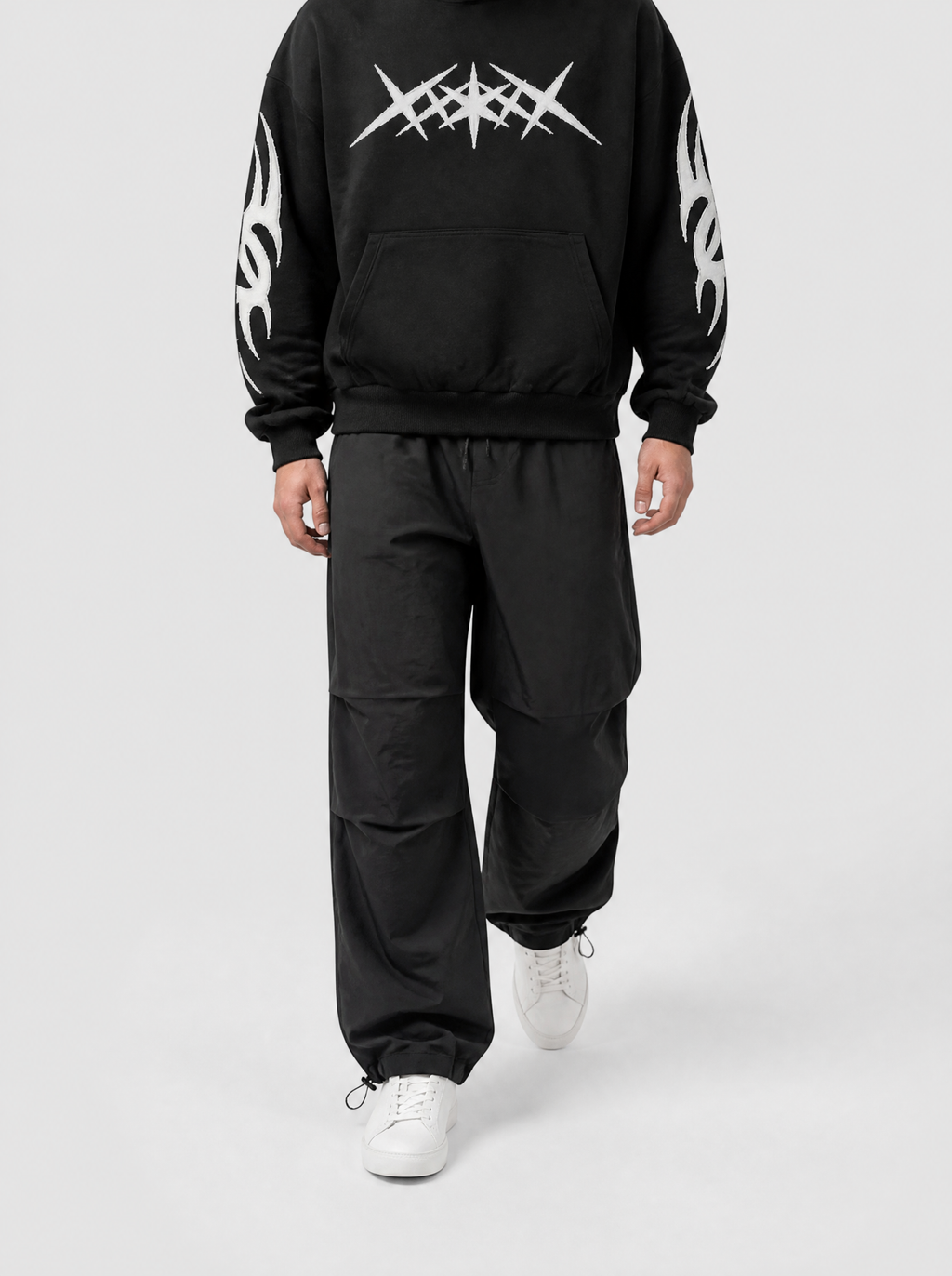 Autre vue | Homme marchant de face en pantalon parachute noir à cordons de serrage aux chevilles et hoodie noir graphique