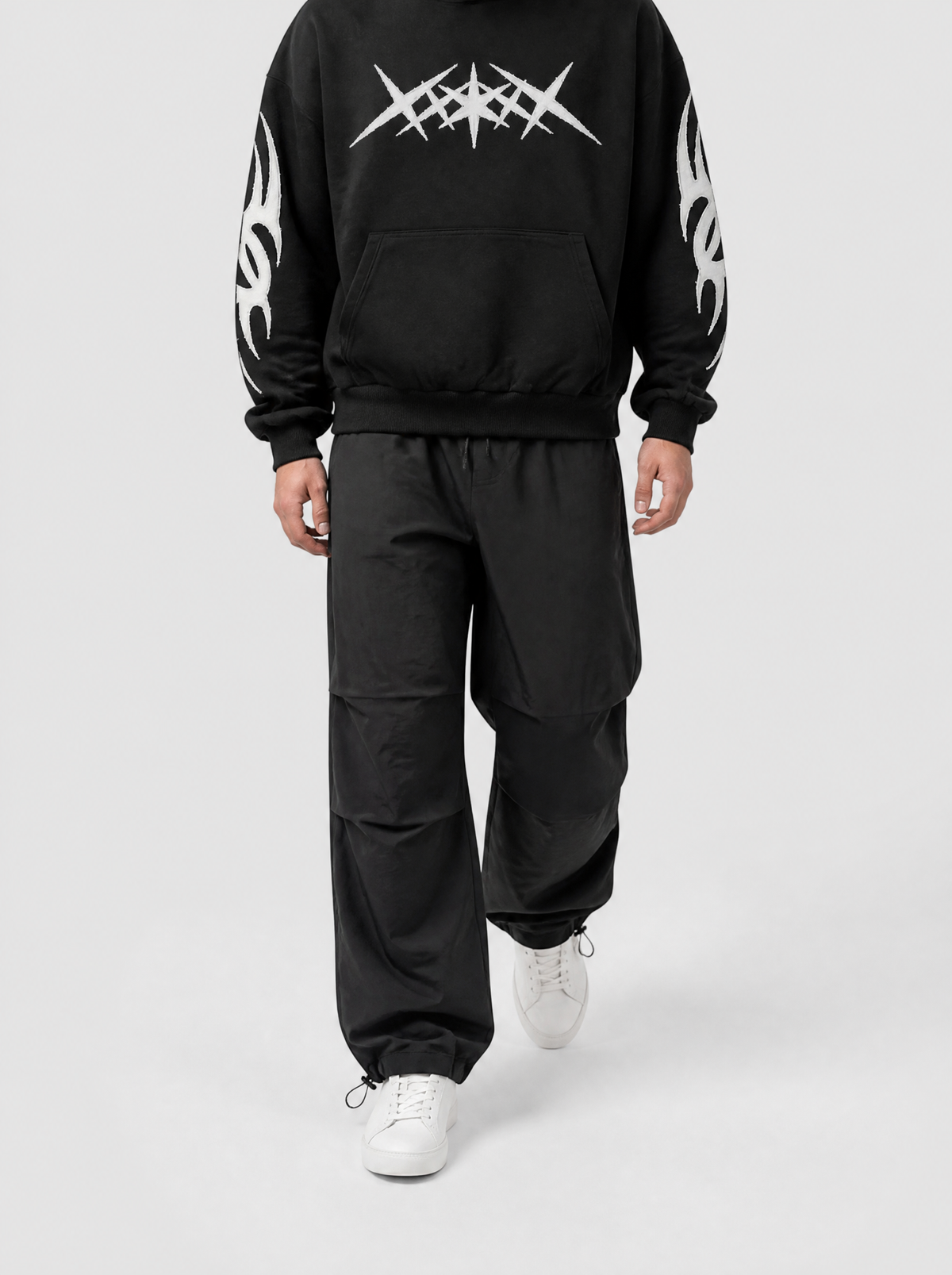 Autre vue | Homme marchant de face en pantalon parachute noir à cordons de serrage aux chevilles et hoodie noir graphique