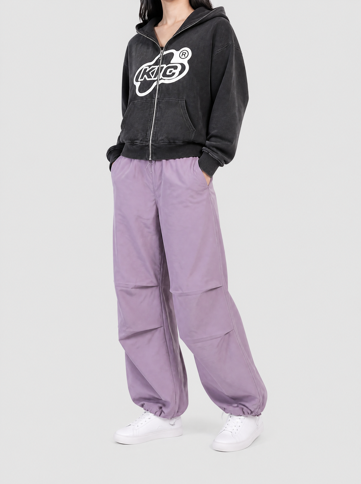 Autre vue | Pantalon parachute lilas en nylon léger à plis aux genoux, porté de trois quarts par une femme avec un hoodie zippé noir