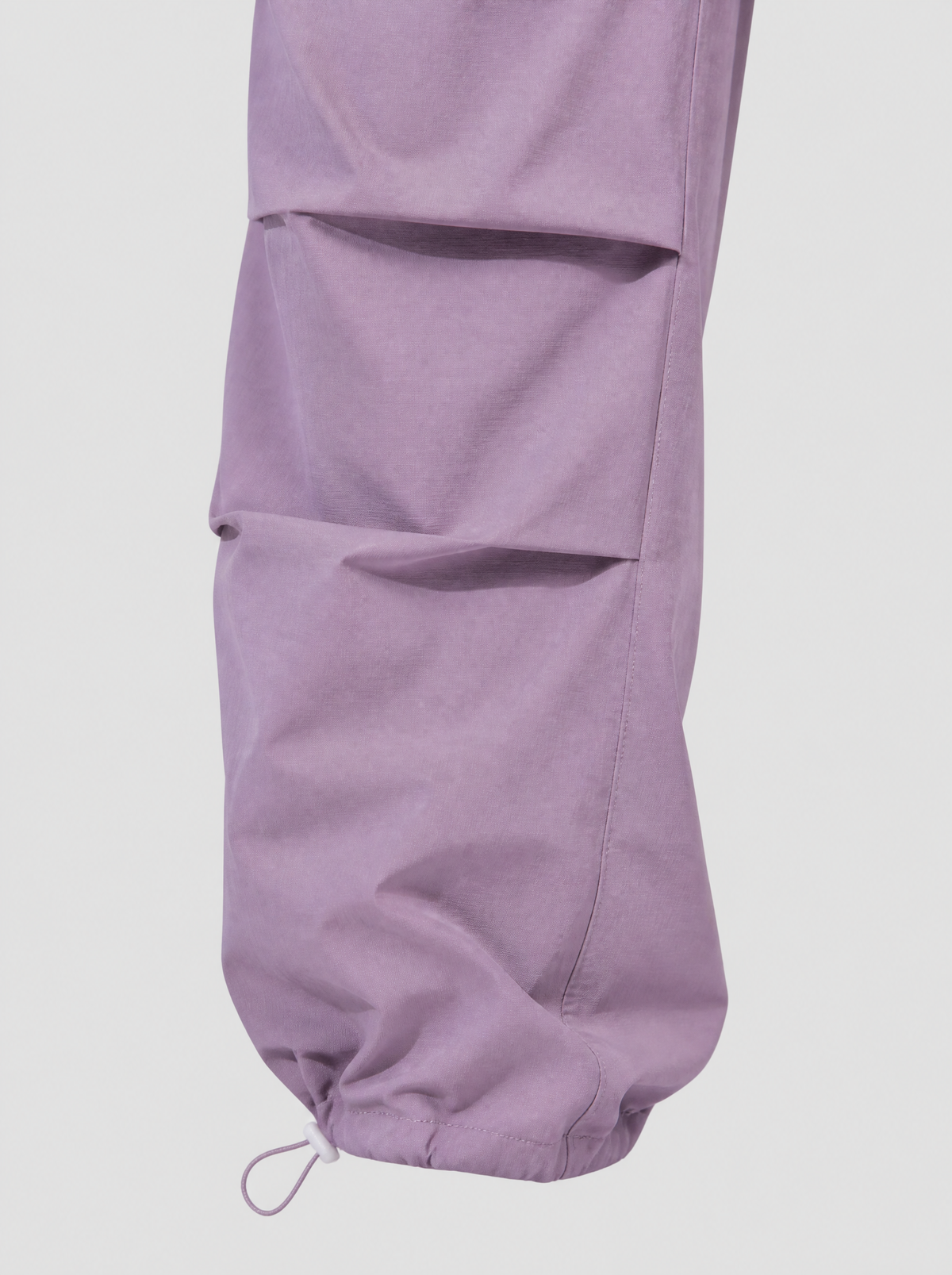 Photo détail | Gros plan sur les plis au genou et le cordon à stoppeur blanc du pantalon parachute lilas