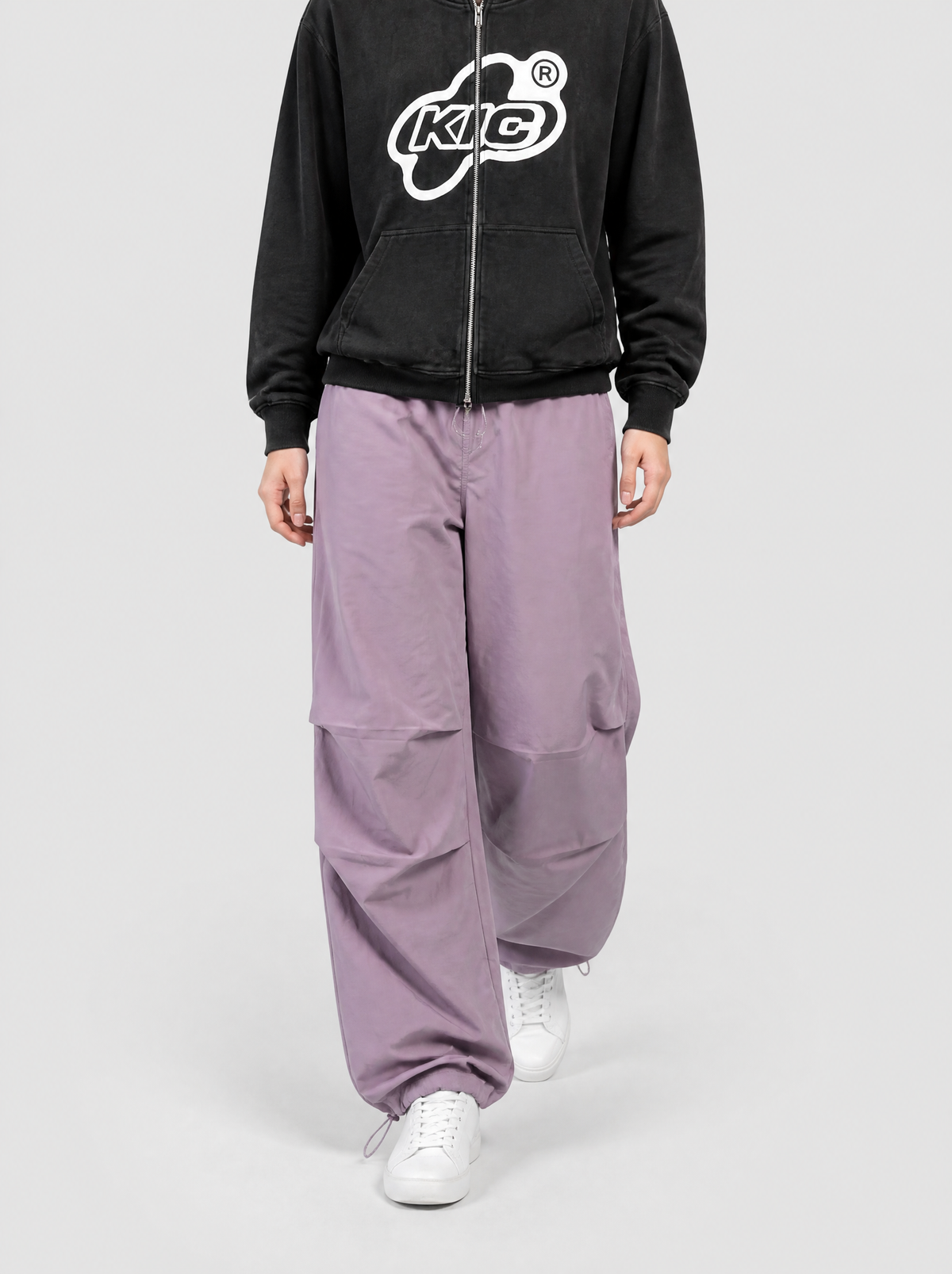 Autre vue | Femme marchant de face en pantalon parachute violet lavande à cordons de chevilles et hoodie zippé noir à logo blanc