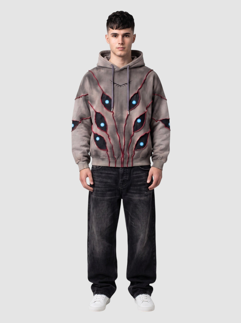 Hoodie oversize beige délavé avec découpes patchwork en forme d'yeux à pupilles bleues et détails de surpiqûres rouges.