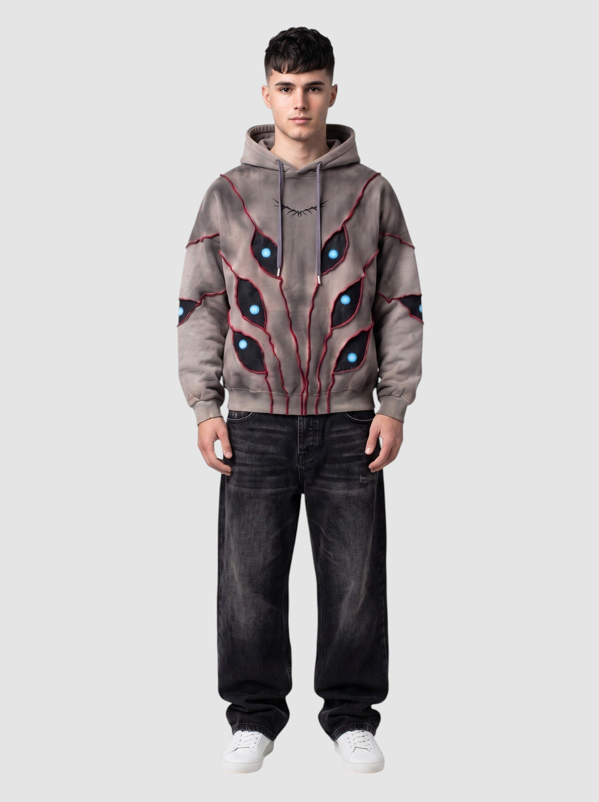Hoodie oversize beige délavé avec découpes patchwork en forme d'yeux à pupilles bleues et détails de surpiqûres rouges.