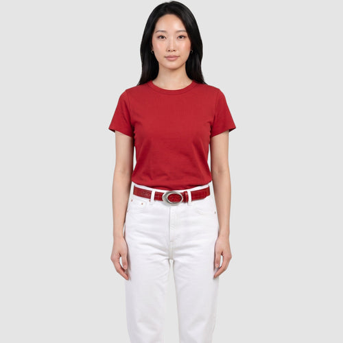 Ceinture rouge en cuir synthétique crocodile avec boucle ovale argentée, portée par un modèle en t-shirt rouge et jean blanc.