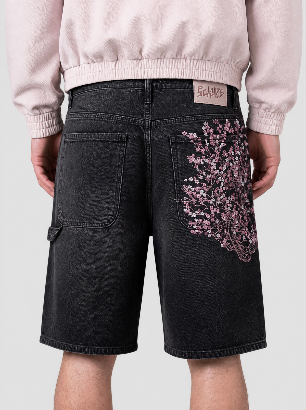 Photo détail | Gros plan sur la broderie de fleurs de cerisier roses et blanches sur la poche arrière du short en jean noir