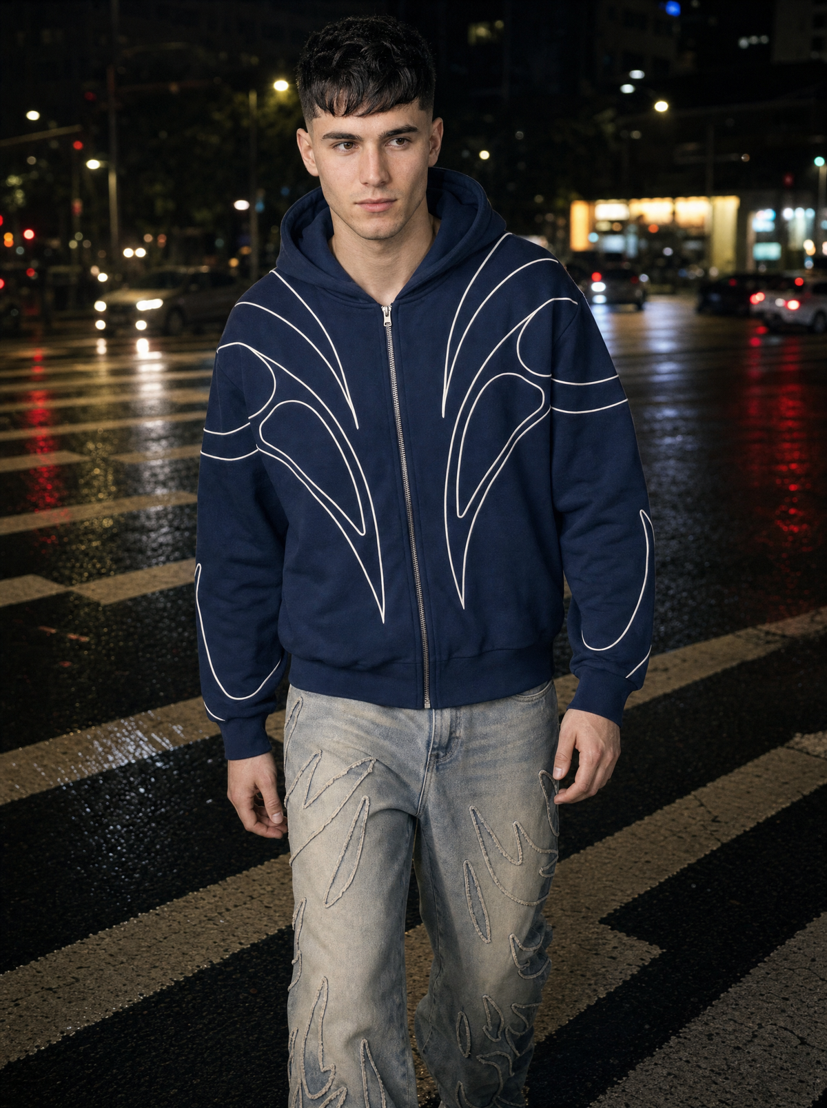 Photo lifestyle | Homme qui traverse un passage piéton la nuit en sweat zippé bleu marine à passepoils blancs et jean délavé à flammes | Variante : Bleu