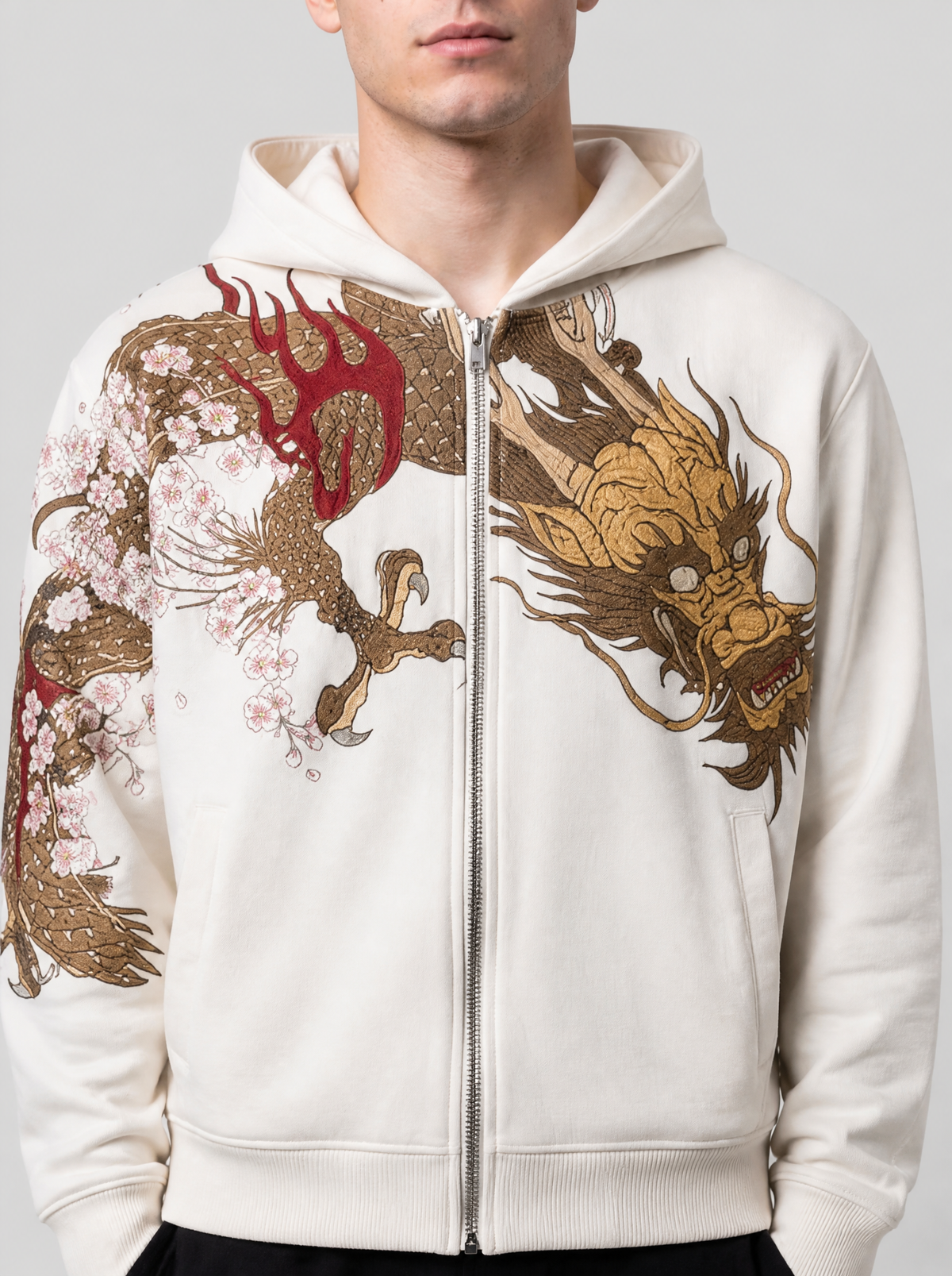 Photo détail | Gros plan sur la poitrine du sweat zippé crème : tête de dragon doré, flammes rouges et fleurs de cerisier de part et d'autre du zip | Variante : Blanc